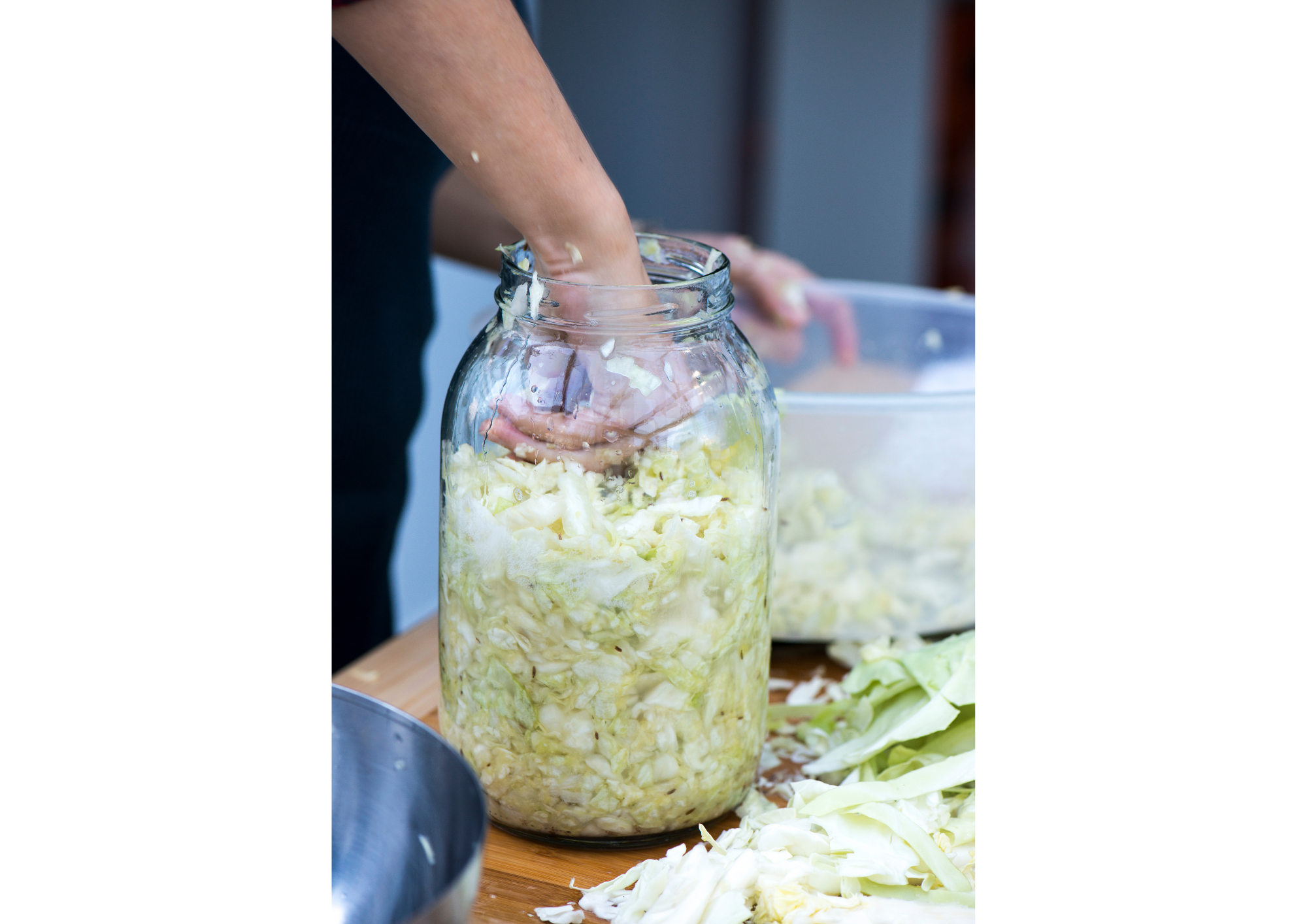 Hands pressing shredded cabbage into a fermentation jar