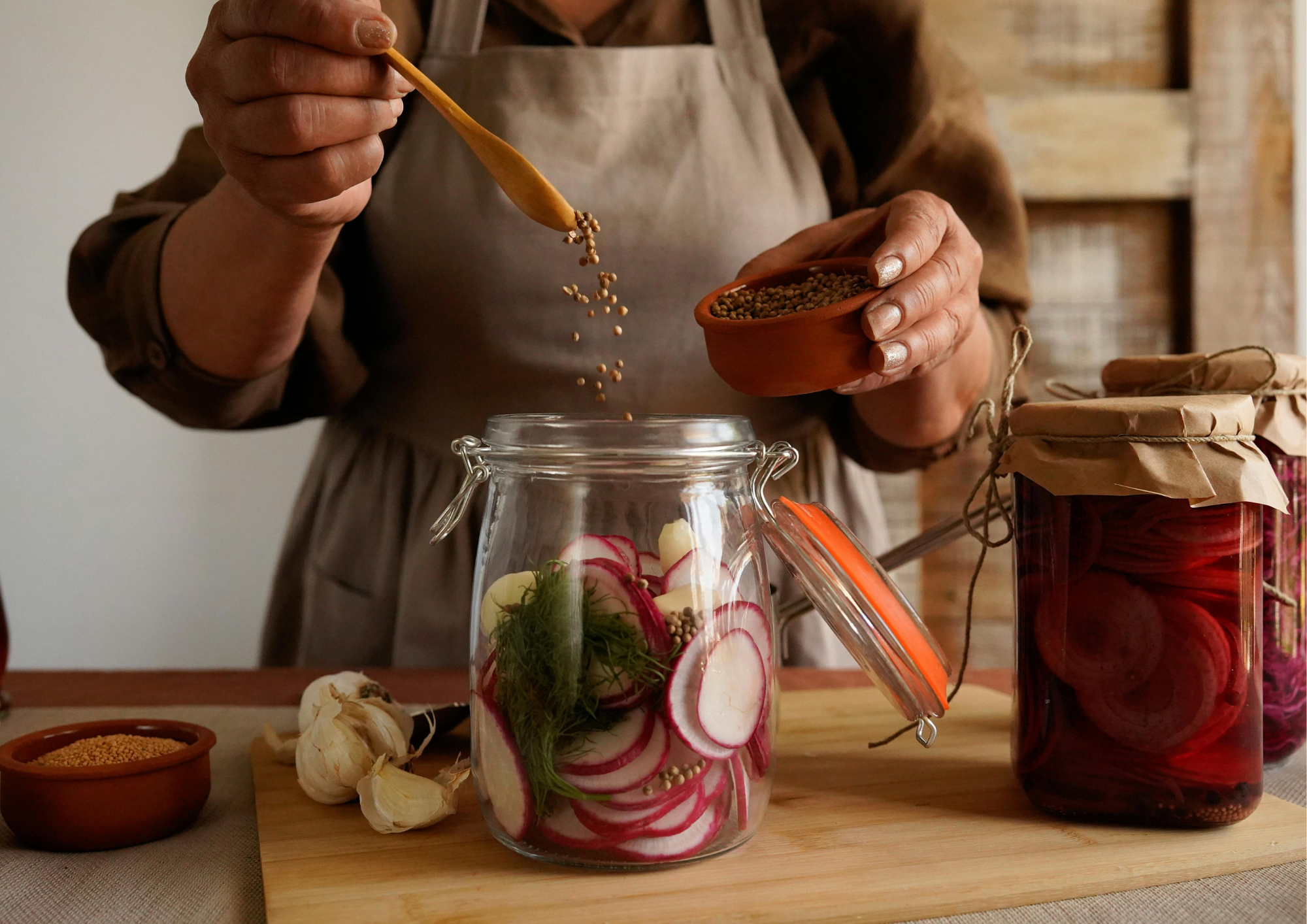 Hands adding spices to a jar before covering vegetables in vinegar brine